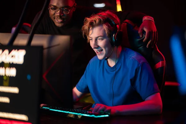 An experienced esports player shows his dark-skinned friend how to play an online video game in a computer club — Stock Photo, Image