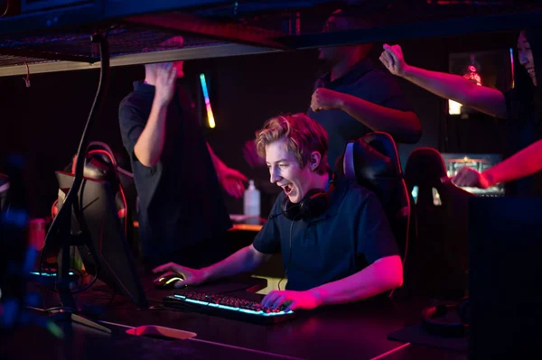 Two guys and a girl in medical masks in a computer club give support to their friend during his game — Stock Photo, Image