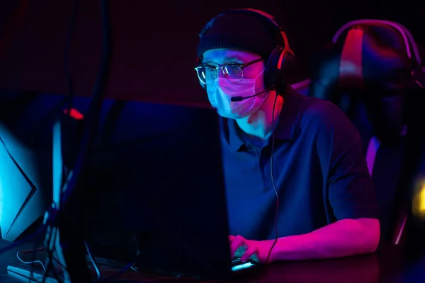 Ospitare un torneo di esport durante una pandemia e una quarantena. Un giocatore di sport in una maschera medica gioca uno sparatutto online su un potente computer da gioco. — Foto Stock