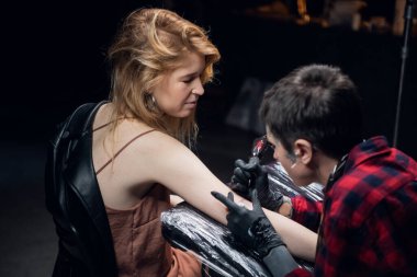 Dövme salonundaki sarışın bir kadın koluna dövme yaptırıyor. Dövmeci kız şeklinde.