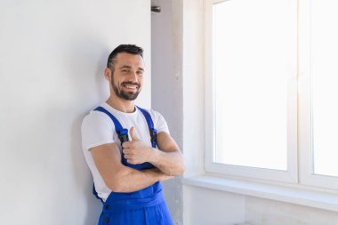 Üniformalı inşaatçı başparmağını gösteriyor ve gülümsüyor