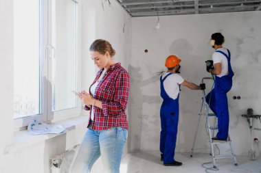 Cep telefonu kullanan kadın istemci, arka planda çalışan inşaatçılar