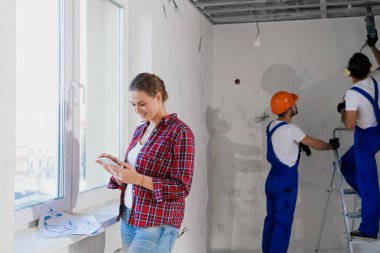 Dairenin sahibi cep telefonu kullanıyor, arka planda üniformalı adamlar çalışıyor.