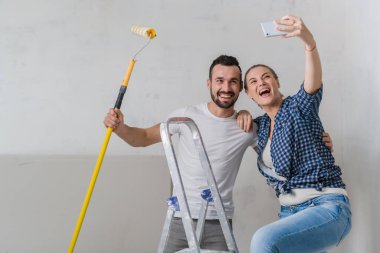 Evli bir çift, onarımlarını yaparken telefonda selfie çeker ve gülümserler.