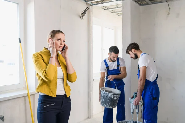 Los constructores están renovando una habitación, una mujer habla por teléfono — Foto de Stock