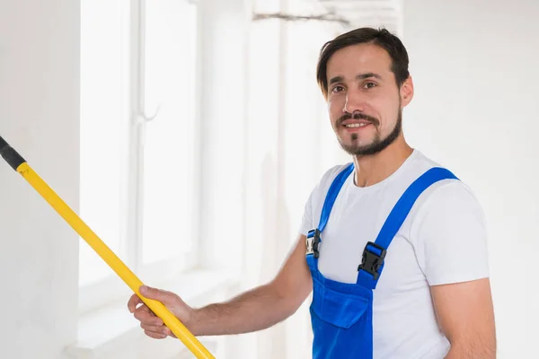 Bonito pintor em macacão pinta a parede com um rolo — Fotografia de Stock