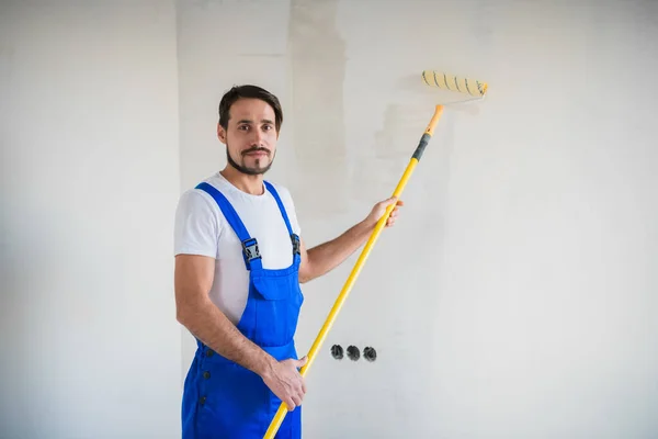 작업복을 입고 벽 가까이에 서서 손에 로울러 를 쥐고 있는 남성 페인트 칠을 하는 모습 — 스톡 사진