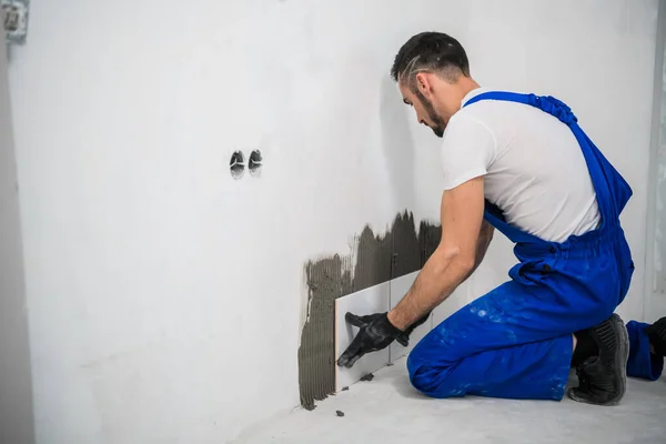 Tiler en overoles pone azulejos en la pared del baño — Foto de Stock