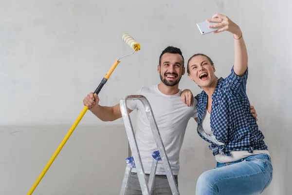 Man in a white shirt and woman taking selfie on the background of the wall with a stepladder and roller — Stock Photo, Image