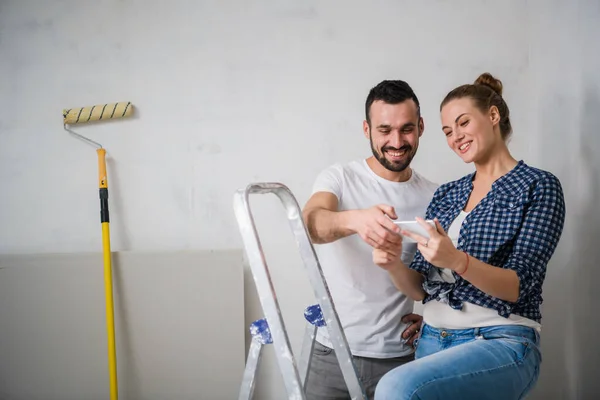 A bearded man and a woman are looking at a photo on a smartphone in an apartment being renovated — Stock Photo, Image