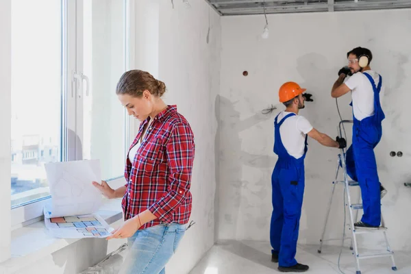 Le client se tient à la fenêtre et examine la disposition de l'appartement, les constructeurs travaillent en arrière-plan Photos De Stock Libres De Droits