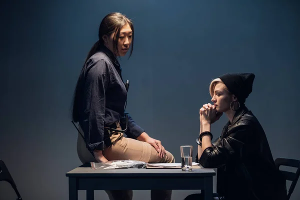 Un investigatore donna siede su un tavolo e interroga un giovane criminale in una stanza degli interrogatori — Foto Stock