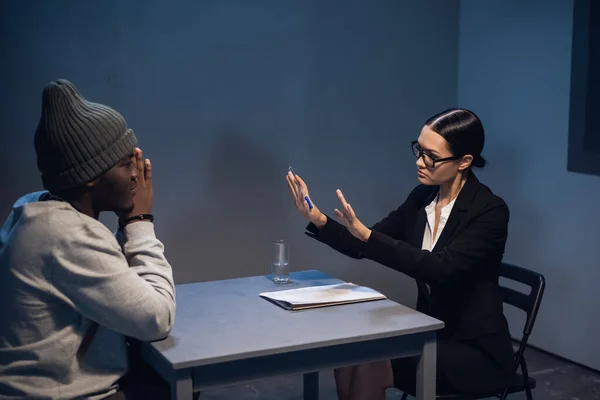 Адвокат молодої дівчини консультує свого клієнта в поліцейському відділенні, чорношкірого чоловіка в кепці і наручниках . — стокове фото