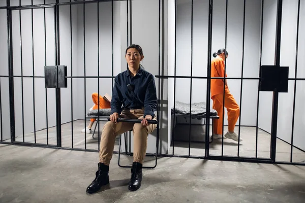 Типовий день у жіночій в'язниці. Набридла жінка-охоронець у формі сидить біля кліток з в'язнями-жінками . — стокове фото