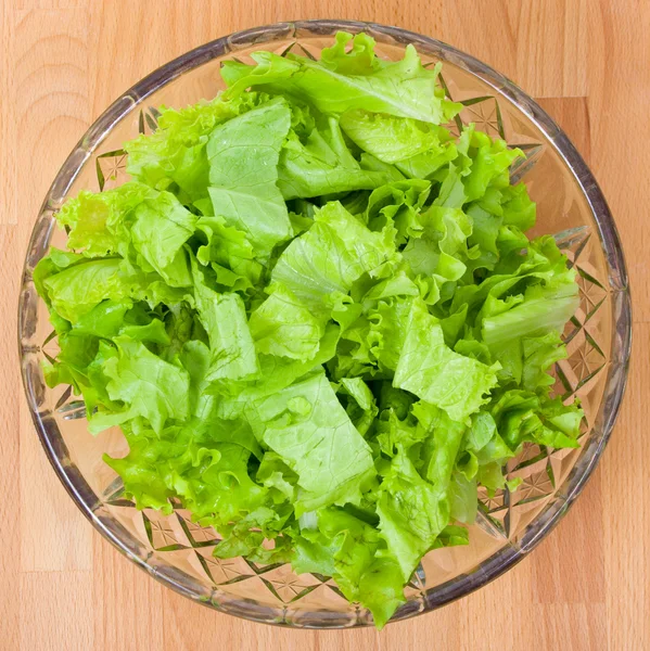 Salade fraîche découpée dans une assiette en verre sur une planche en bois — Photo