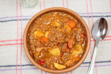 Ev yapımı mercimek güveci, domates, İspanyol sucuğu, masa örtüsü üzerine et ve patates.