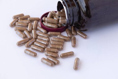 Kahverengi kapaklı kehribar plastik şişe, beyaz bir yüzey üzerine dökülen ilaç veya diyet takviyesi bir sürü hap ile açıldı
