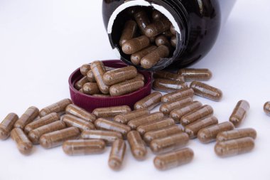 Kahverengi kapaklı kehribar plastik şişe, beyaz bir yüzey üzerine dökülen ilaç veya diyet takviyesi bir sürü hap ile açıldı