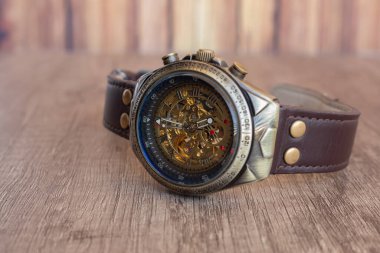 Bronz, çelik, lacivert iç halkadan ve ahşap bir tahtanın üzerindeki kahverengi deri örgüden yapılmış Steampunk tarzı kol saati. Saatin dahili makinesini görebilirsiniz..