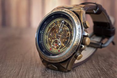 Bronz, çelik, lacivert iç halkadan ve ahşap bir tahtanın üzerindeki kahverengi deri örgüden yapılmış Steampunk tarzı kol saati. Saatin dahili makinesini görebilirsiniz..