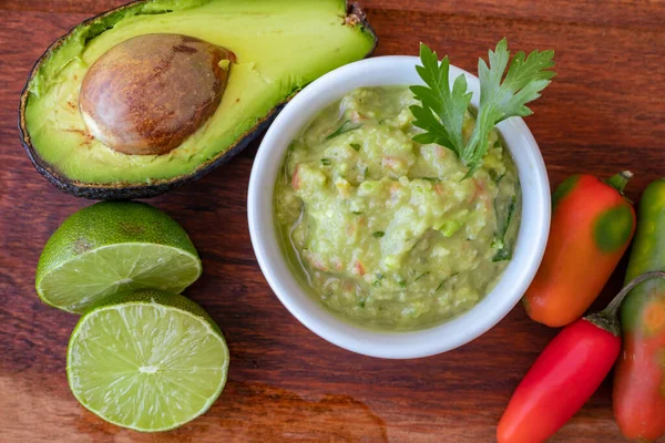 Yarım avokado, biraz acı biber ve ahşap bir tahtada limon ve guacamole soslu kase.