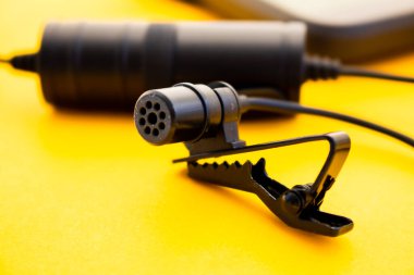 Renkli bir yüzeye yakın plan Lavalier ya da klapa mikrofon. Bağlayıcı ya da tutacağının ayrıntıları, mikrofon güç bankası. Kullanışlı nesne kavramı, ses üretimi,