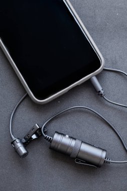 Siyah bir yüzeye yakın plan Lavalier ya da klapa mikrofon. Klipsin veya sütyenin ayrıntıları, Power Bank ve cep telefonunun konveksiyonu.