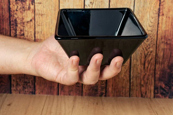 Mano Sosteniendo Cuenco Vacío Negro Cuadrado Sobre Fondo Madera 45º — Foto de Stock