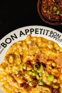 Locro 'nun servis ettiği beyaz tabak, geleneksel Arjantin ve Güney Amerika yemekleri. Siyah arka plan ve acı soslu küçük kase. Hava görünümü.