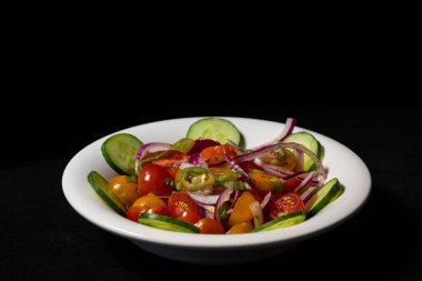 İki renkli kirazlı domates salatası, salatalık, kırmızı soğan ve masadaki eski bir kasede servis edilen acı biber. siyah arkaplan