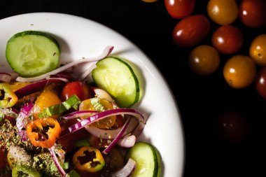 İki renkli kirazlı domates salatası, salatalık, kırmızı soğan ve masadaki eski bir kasede servis edilen acı biber. siyah arkaplan