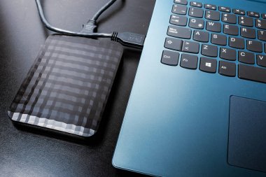 USB kablosu olan harici sabit disk siyah bir yüzeydeki dizüstü bilgisayara ya da dizüstü bilgisayara bağlı. kavram teknolojisi