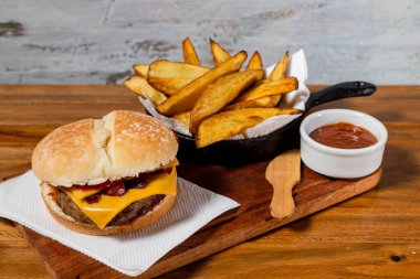 Çedar peynirli lezzetli burger ve ev yapımı ekmek üzerine ızgara domuz pastırması yanında da patates ve ev yapımı barbekü sosu..