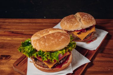 Pastırma ve çedar peynirli leziz hamburgerler ve marul, domates, kırmızı soğan ve domuz pastırması ile tahtadan bir yüzeyde tohum ve ketçap ile ev yapımı ekmek..