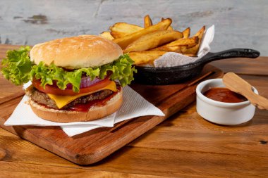 Çedar peynirli lezzetli hamburger, marul, domates, kırmızı soğan halkaları ve ev yapımı ekmek üzerine ızgara domuz pastırması yanında da patates ve ev yapımı barbekü sosu..