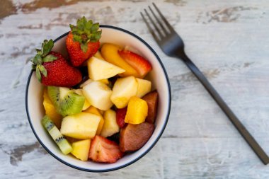 Doğal ve sağlıklı meyve salatası. Kırsal bir yüzeyde turuncu bir kapta. Sağlıklı Gıda Konsepti, Sağlıklı Yaşam. Orta görünüm.