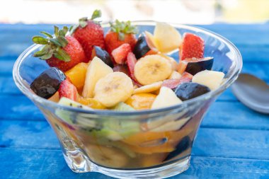 Doğal ve sağlıklı meyve salatası, şeffaf cam bir kâse içinde portakal seti, kırsal ve mavi bir yüzey üzerinde. Sağlıklı Gıda Konsepti, Sağlıklı Yaşam. 45 derecelik görünüm, yazma alanı