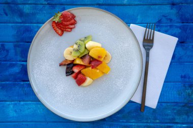 Doğal ve sağlıklı meyve salatası, turuncu seti ve kırsal mavi bir yüzeyde sunum tabağı. Sağlıklı Gıda Konsepti, Sağlıklı Yaşam. Zirve görünümü.