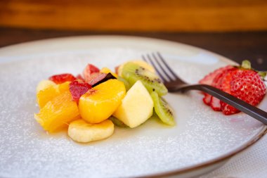 Doğal ve sağlıklı meyve salatası ve turuncu seti, kırsal siyah bir yüzeyde sunum tabağında sunulur. Sağlıklı Gıda Konsepti, Sağlıklı Yaşam. 45 deg. görünüm