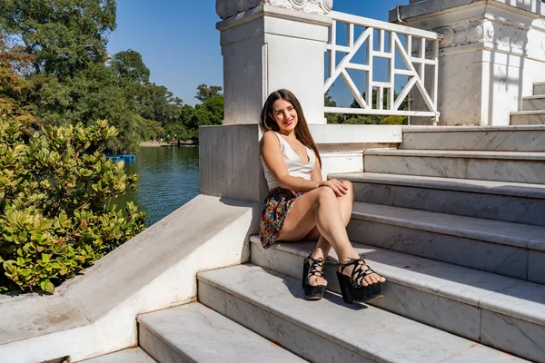 Beautiful young Latina woman sitting on the steps of a white marble staircase resting in the sun.