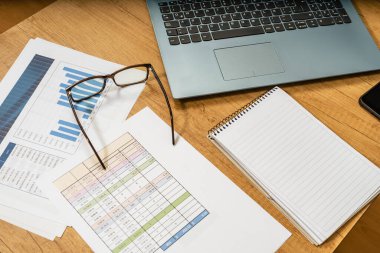 Evde çalışma masasında kalem, kağıt, fatura, çizelge, gözlük, bilgisayar ve hesap makinesi var. Evde çalışma kavramı, çek hesapları, konut ekonomisi.