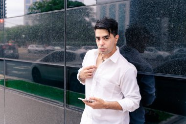 Genç İspanyol ya da Latin bir adam bir binanın duvarına yaslanıyor..