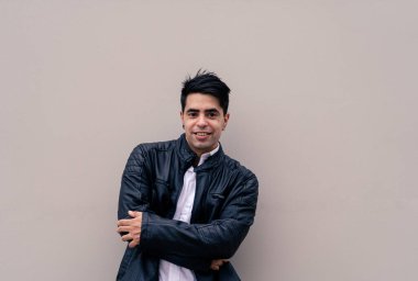 Düz renkli bir duvara yaslanmış genç bir Latin 'in yarım boy fotoğrafı. Şehir kıyafetleri.