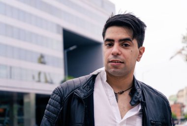 Siyah ceketli, beyaz tişörtlü, modern binalı çekici bir Latin..