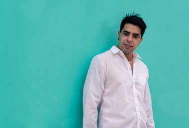 Düz renkli bir duvara yaslanmış genç bir Latin 'in yarım boy fotoğrafı. Şehir kıyafetleri.