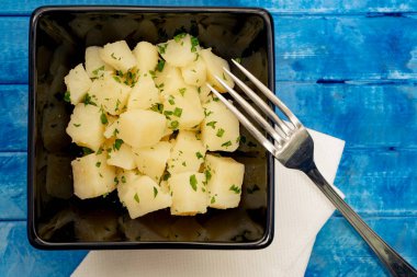 Patates ve maydanoz salatası siyah bir kasede, mavi bir arka planda..