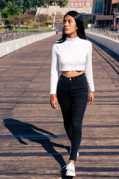 Beautiful Latin woman with black hair walking on a bridge with a wooden floor. Casual clothes. travel concept.