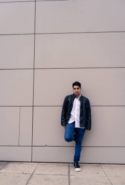 Sade renkli bir duvara yaslanmış genç bir Latin 'in tam vücut fotoğrafı. Şehir kıyafetleri.