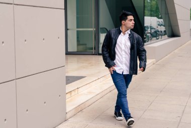 Genç Latin bir adam sokakları gözetlerken ya da izlerken binadan çıkıyor. Modern giysiler.