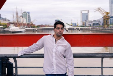 Arka planda eski bir liman olan korkuluklara yaslanan zarif Latin bir adam...